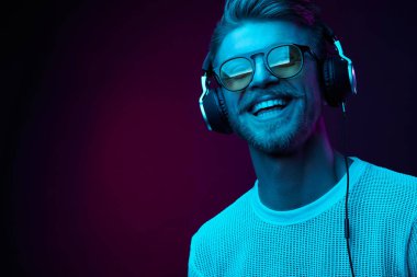 Neon kulaklıklar, güneş gözlüğü, beyaz t-shirt sakallı gülümseyen adam portresi. Müzik 