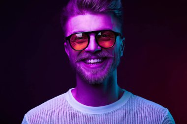 Man modeli bıyık ve sakal turuncu güneş gözlüğü ve beyaz t-shirt ile gülümseyen neon ışık portresi 
