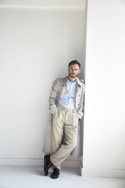 Yakışıklı adam karanlık sakal ve saç, suni ışık palto, gömlek, bej pantolon ve siyah ayakkabı moda portre. 