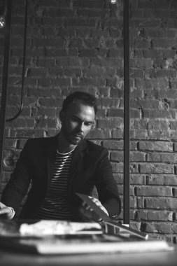 Koyu saç ve sakal ceketli ile şık yakışıklı siyah beyaz portre. Onun iş yerinde, iş adamı. Arka plan üzerinde tuğla duvar