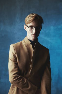 Kızıl saçlı ve çilli ile genç erkek model karanlık stüdyo portre. Kahverengi ceket ve gözlük renksizdir. Mavi ışık ve arka plan.
