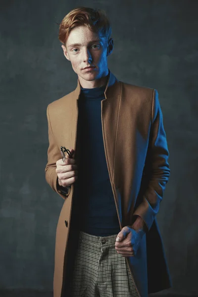 赤い髪とそばかすの若い男性モデルのスタジオの肖像画 Weared 茶色のコートで 格子縞ズボン メガネを手に — ストック写真