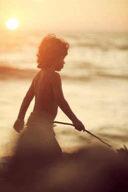 Kıvırcık saçlı ile sahilde yürüyüş Mowgli çocuk elinde sopa. Golden sunset