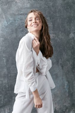 Esmer kadın model beyaz gömlek, üst ve pantolon poz gülümseyerek. Atış, gri arka plan stüdyo 