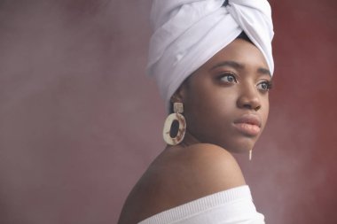 Beyaz baş kravat, beyaz elbise ve büyük küpeler genç kadın güzellik portresi. Kırmızı arka plan, sahnede duman  