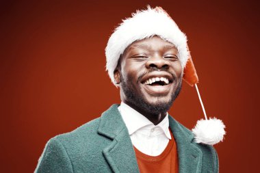 Santa claus şapka, yeşil ceket, kırmızı kazaklı neşeli adam portresi. Ateş, kırmızı arka plan stüdyo