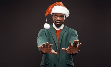 Modern Noel Baba. Yeşil ceket ve santa çantası ile kırmızı kazaklı adam elinde gülümseyerek. Atış, arka plan siyah stüdyo