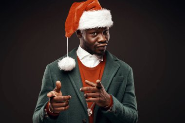 Modern Noel Baba. Yeşil ceket ve santa çantası ile kırmızı kazaklı adam elinde gülümseyerek. Atış, arka plan siyah stüdyo