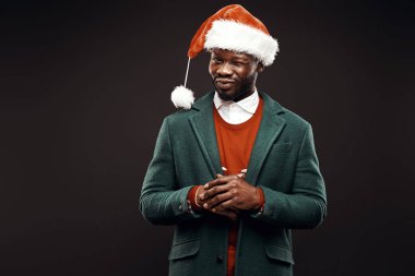 Modern Noel Baba. Yeşil ceket ve santa çantası ile kırmızı kazaklı adam elinde gülümseyerek. Atış, arka plan siyah stüdyo