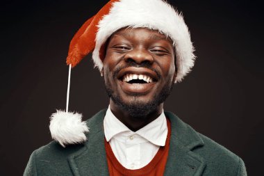 Modern Noel Baba. Yeşil ceket ve santa çantası ile kırmızı kazaklı adam elinde gülümseyerek. Atış, arka plan siyah stüdyo