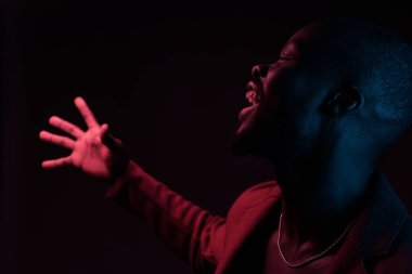 Profilde sakallı yakışıklı gülümseyen adam portresi. Stüdyo çekim, siyah arka plan, pembe ve mavi ışık, neon