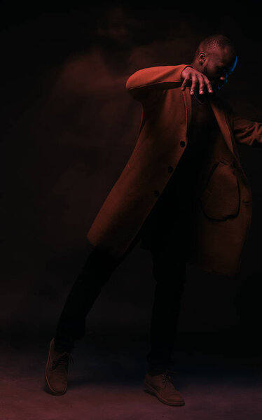 Full length portrait of dancing shirtless man in brown coat and jeans. Studio shot, motion, long exposure