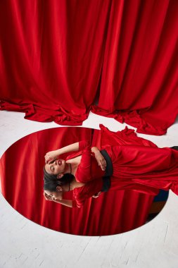 Şık ve seksi güzel genç esmer elbiseli kadın büyük yuvarlak ayna döşeme kırmızı ipek gibi. Arka plan üzerinde kırmızı perde