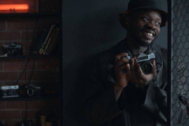 Koyu siyah palto ve kova şapka, genç moda adam elinde kamerayla portresi.