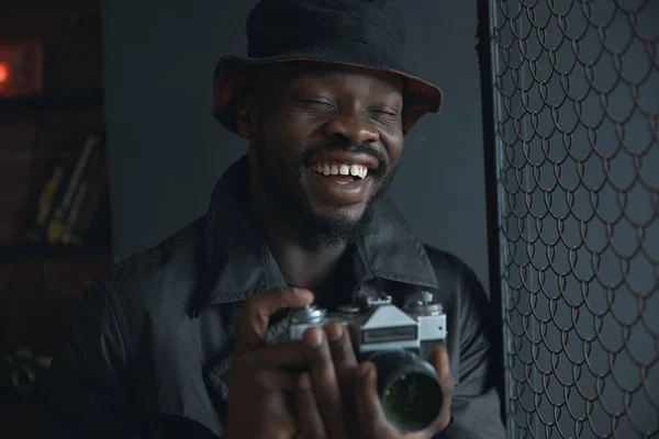 黑色风衣和水桶帽的年轻时尚男子的黑暗肖像 手里拿着相机 — 图库照片