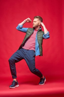 Erkek manken sıradan kıyafetlerle poz. Moda portre, stüdyo çekimi, kırmızı arka plan