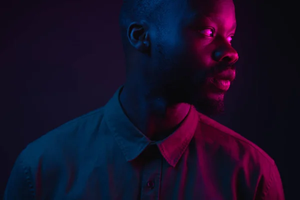 Dark neon portrait of young man with beard, wearer in shirt. Pink and blue light. Technology