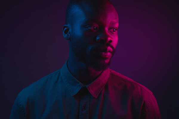 Dark neon portrait of young man with beard, wearer in shirt. Pink and blue light. Technology