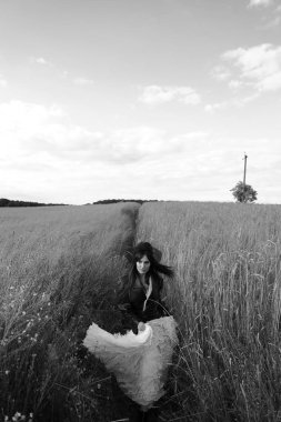 Deri ceketli, siyah şapkalı, beyaz elbiseli, çimenlerde yürüyen güzel genç kadının siyah beyaz portresi. 