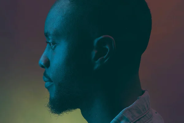 Neon portrait in profile. Black man with beard in dark blue, green and violet light