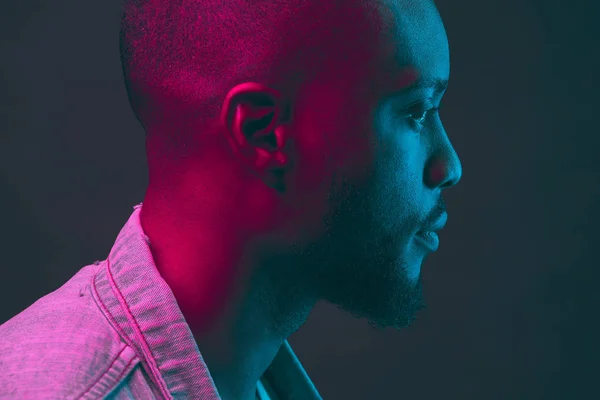 Neon portrait in profile. Black man with beard in dark blue, green and violet light