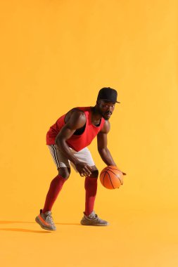 Basketbol oynarken kırmızı gömlek, siyah şapka ve gri şort siyah adam tam uzunlukta portre. Stüdyo, sarı arka plan