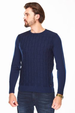 sakallı ve koyu saçlı adam rombs ve koyu kot ile koyu mavi kazak beyaz bir arka plan üzerinde duruyor, o kolunda altın bir saat var ve uzak görünüyor