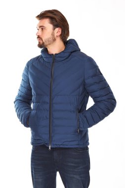 sakallı ve koyu saçlı adam koyu mavi ceket ve kot pantolon beyaz bir arka plan üzerinde duruyor, o ceplerinde sol yönde eller görünüyor