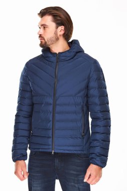 sakallı ve koyu saçlı adam koyu mavi ceket ve kot beyaz bir arka plan üzerinde duruyor, o sol yönde bakar 