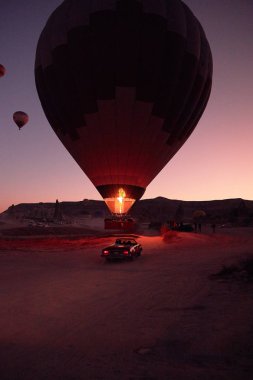 Zeminde insanlar olan büyük bir balon ve arka planda kumlu tepeler ve birkaç küçük hava balonu var.
