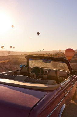 Mavi gökyüzünün arka planında deri kaplı kırmızı retro cabriolet ve kum tepelerinin üzerinde balonlar.