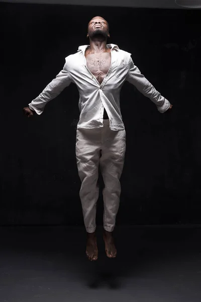 full-height photo of black man in linen suit on black background he is jumping up and looks to the light