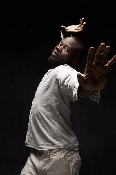 portrait of black man in linen suit on black background he raises his hand in front of him and above his head and looks into the camera