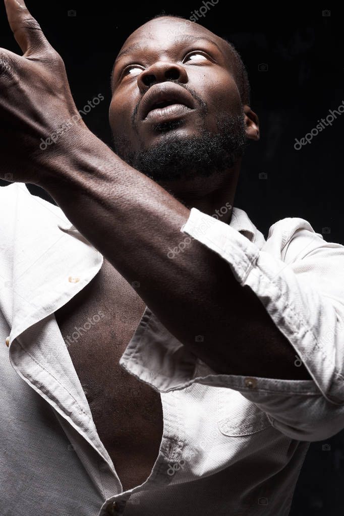 portrait of black man in linen suit on black background he raises his hand in front of him and looks up to the left