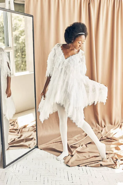 full-length photo of a dark-skinned girl in a white boho style dress, white tights, on a brown fabric background near the mirror in full growth