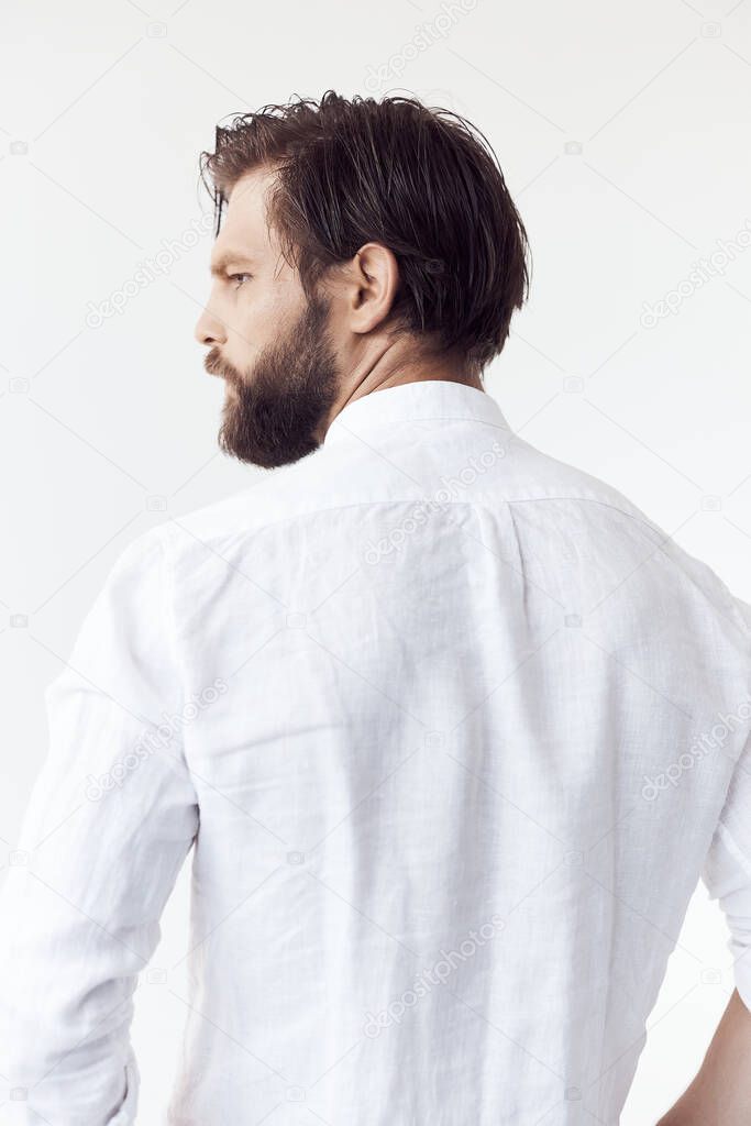 portrait photo from the back on white cyclorama of a handsome bearded man with brown hair, he is wearing a white linen shirt and  looks away