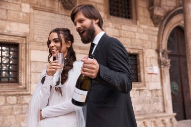 Yeni evli çift, duygusal ve mutlu bir şekilde şampanyalarını yudumluyor. Eski kasabadaki düğün onuruna, kadın beyaz elbise giyiyor, adam ise klasik siyah takım elbise giyiyor.