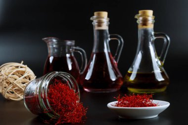 Cam şişede kurumuş safran iplikler ve siyah arka planda yağ özü..