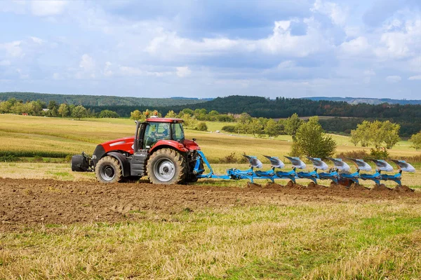 Um trator com um grande arado arado arado um campo. Trator com fixação agrícola . — Fotografia de Stock