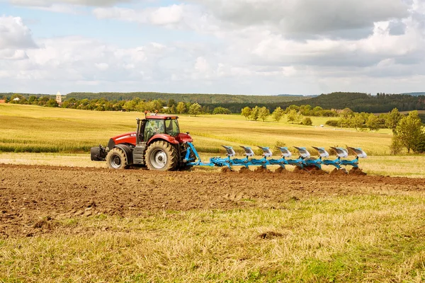Опахать землю. Фермер в красном тракторе готовит землю с плугом для посева — стоковое фото