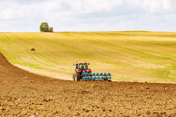 Опахать землю. Фермер в красном тракторе готовит землю с плугом для посева — стоковое фото