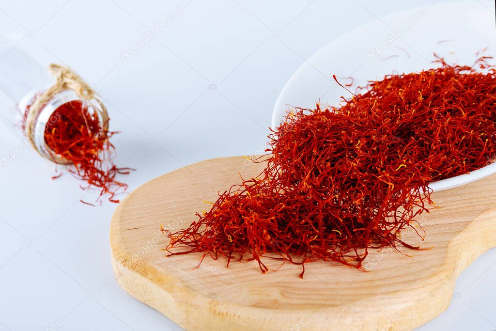 Dry Saffron Spice on Plate on white Background. Wooden board. The use of saffron in cooking, medicine, cosmetology.