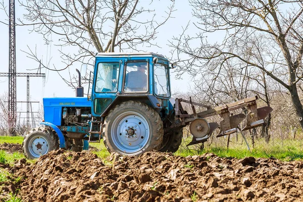 Uzhhorod, Ukrajina, 8. dubna 2020: Farmář v modrém traktoru připravuje půdu s pluhem k setí — Stock fotografie