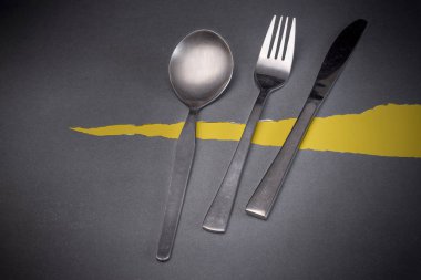 Gri ve sarı arka planı olan çelik çatal bıçak takımı.