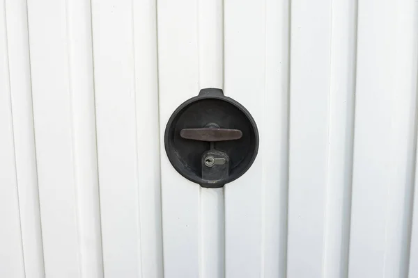lock of a white automatic garage door with manual opening swivel crank
