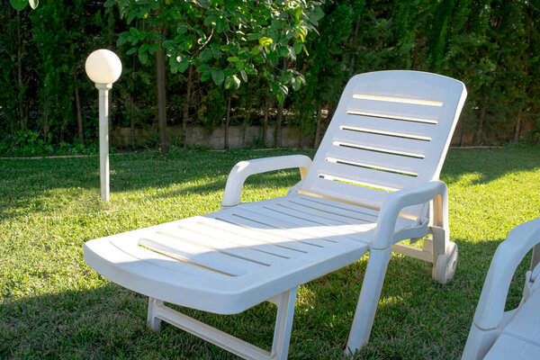 Portable and reclining plastic lounger for sunbathing and resting, placed on the lawn, with a lantern for lighting and in a place with greenery