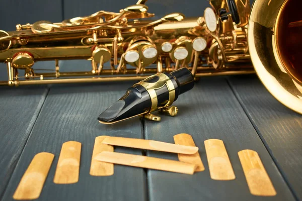 saxophone mouthpiece with metal clamp and gold adjustment hardware, with replacement reeds and instrument body on gray wooden background