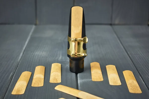 Saksafon ağızlığı ve sazlık, klemp ve altın donanımla birlikte gri ahşap arka planda yeni kamışlarla.