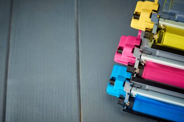 Side view of magenta, cyan and yellow toner for color laser printers stacked on gray wooden background clipart