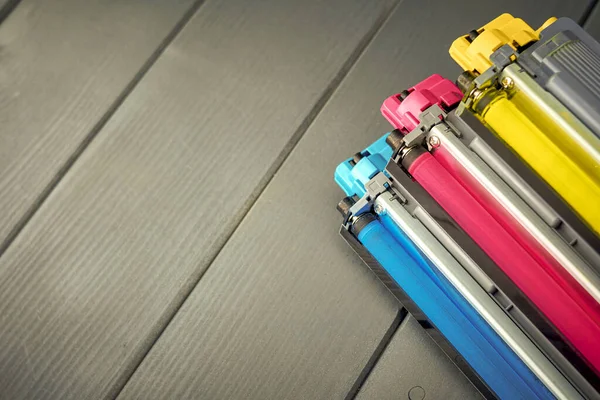 Three used toner cartridges in a color laser printer on gray wooden background for recycling